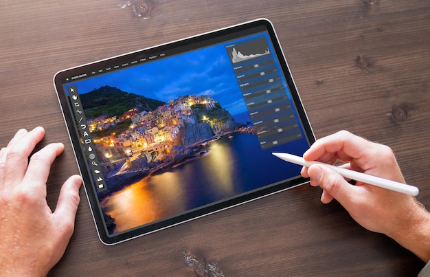 A close-up shot of a tablet screen showing the interface of a photo editing app, with various filters and adjustment options displayed. A stylus pen is touching the screen, indicating precise editing.