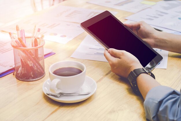A person using a budgeting app on a tablet while researching vacation destinations on a laptop, with a coffee cup and travel brochures on the table.