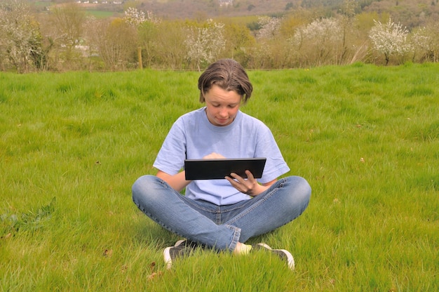 A person studying English with a language learning app on a tablet while sitting in a park on a sunny day. The scene captures the flexibility and convenience of studying outdoors.