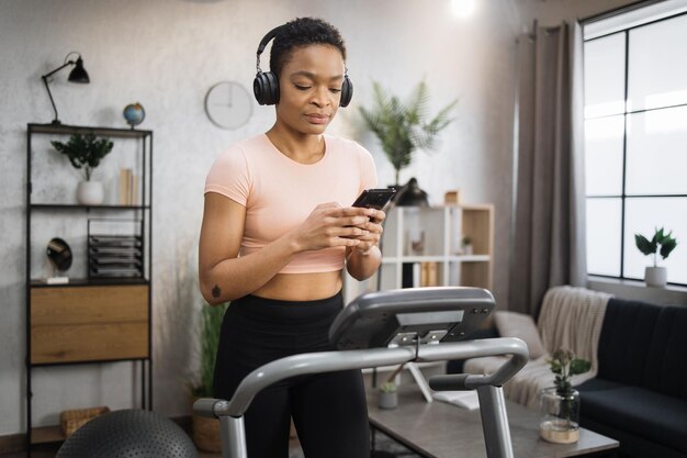 A person using the Nike Training Club app on their phone while exercising at home, with workout equipment in the background