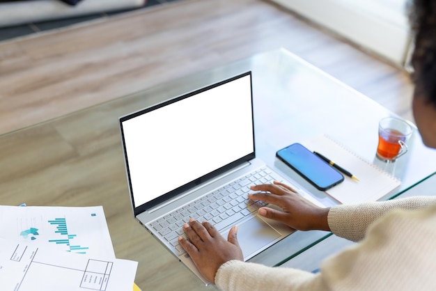 A person sitting at a desk, using a laptop and a smartphone simultaneously. The laptop displays a spreadsheet with financial data, and the smartphone screen shows a budgeting app interface.