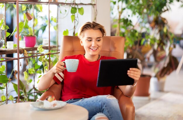 A person happily using a language learning app on a tablet while sitting in a cafe, with a cup of coffee and a notebook nearby. Focus on the screen and the person's positive expression.