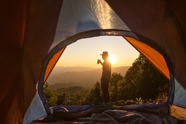 A close-up shot of a traveler pitching a tent in a scenic Brazilian campsite, surrounded by lush greenery and mountains in the background. The focus is on the tent and the natural beauty of the campsite.