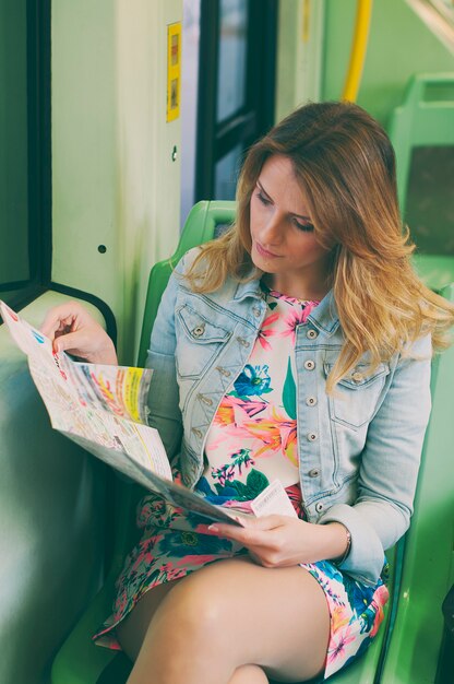 A close-up shot of a woman consulting a map while sitting inside a brightly colored bus in Salvador, Bahia, Brazil. Other passengers are blurred in the background.