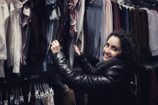 A person holding up a stylish second-hand jacket in front of a clothing rack, showcasing the quality and fashion appeal of used items. The focus is on the texture and design of the jacket, emphasizing its potential value and desirability.